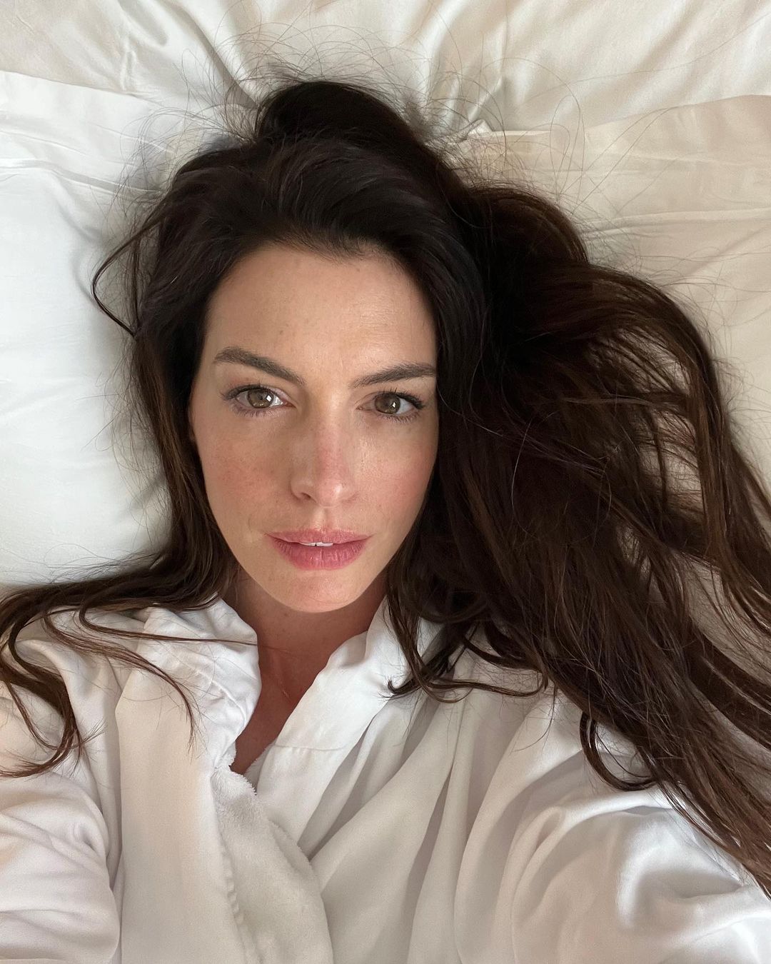 Anne Hathaway lying on the bed in a white button-down shirt